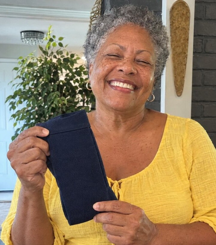 Woman over 60 at home on her sofa wearing Comfyso Premium Bamboo Wide Compression Socks in True Navy, holding a spare pair.