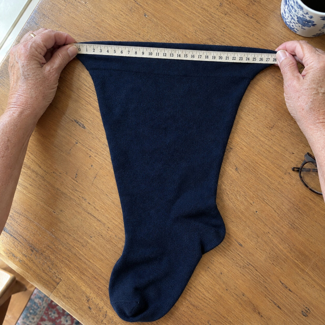 Hands stretching the top of a Comfyso Bamboo knee-high sock across a tape measure to 28 inches.